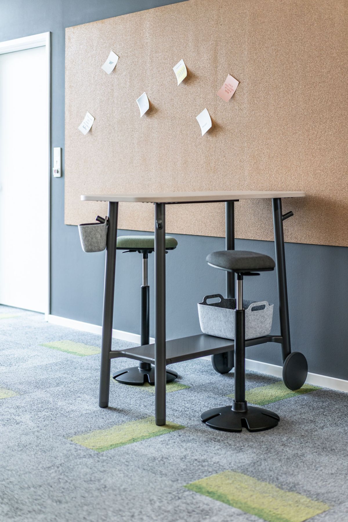 Zwei Steh-Sitzhocker mit Stehtisch vor großer Pinnwand